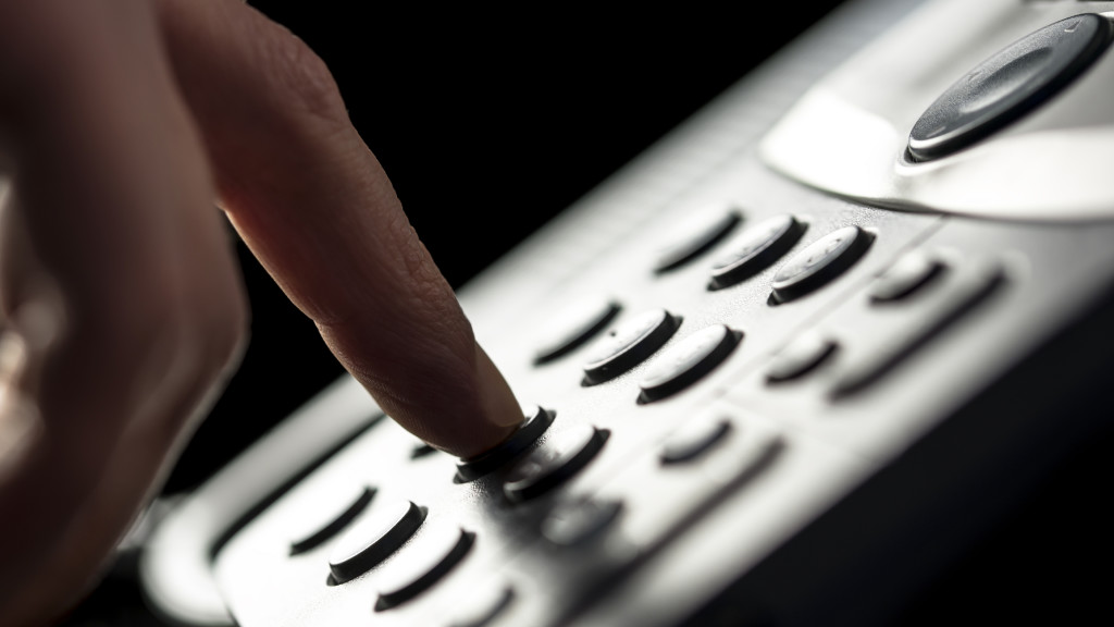 Closeup of the finger of a businessman making a call on a landline telephone pressing the buttons on the keypad to dial the number.  Companies utilizing VoIP experience multiple benefits in the work environment.